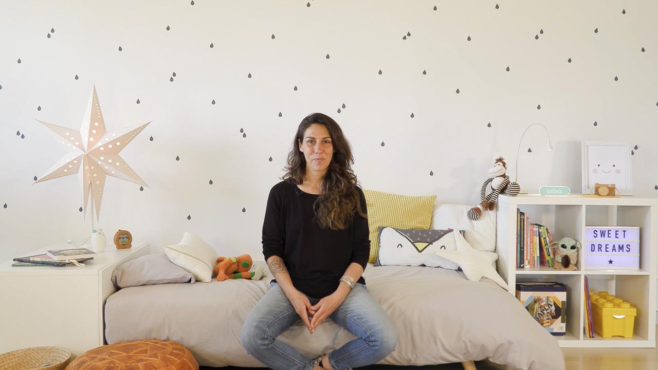 Cris Moe sentada en una cama en una habitación infantil hablando sobre el sueño del bebé. Portada del curso